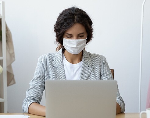 Frau mit Maske am Rechner: Stellenanzeigenschaltung in Krisenzeiten