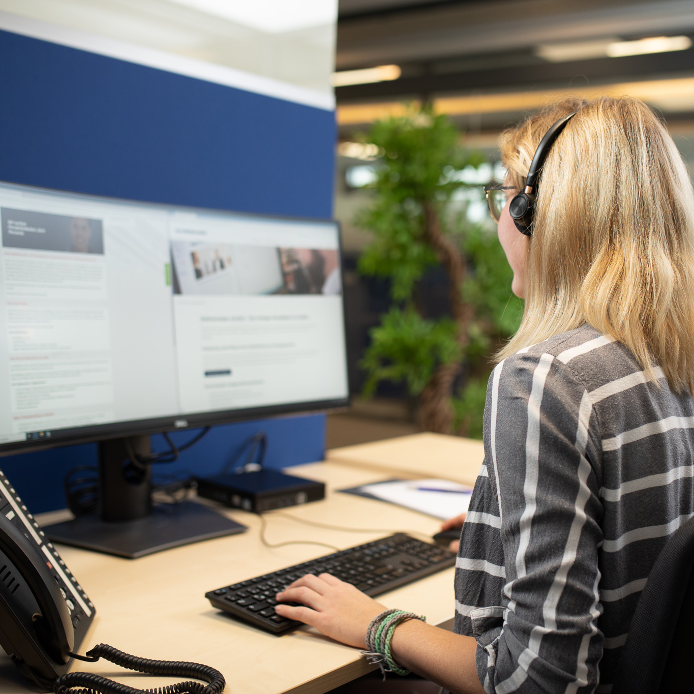 Mitarbeiterin mit Headset pflegt Stellenanzeigen im Corporate Jobboard am Monitor